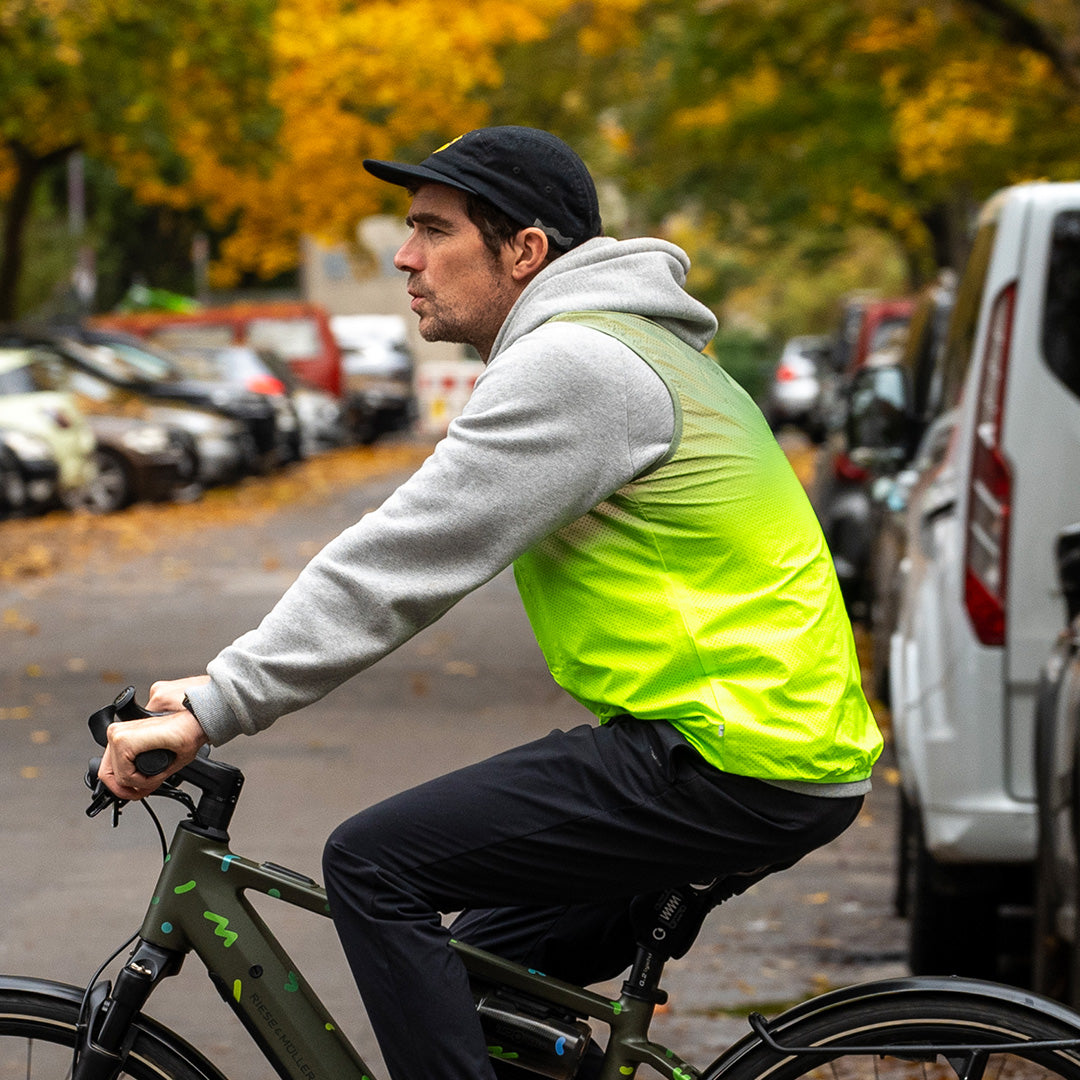 Man riding bicycle and wearing reflective vest in autumn background with cars
