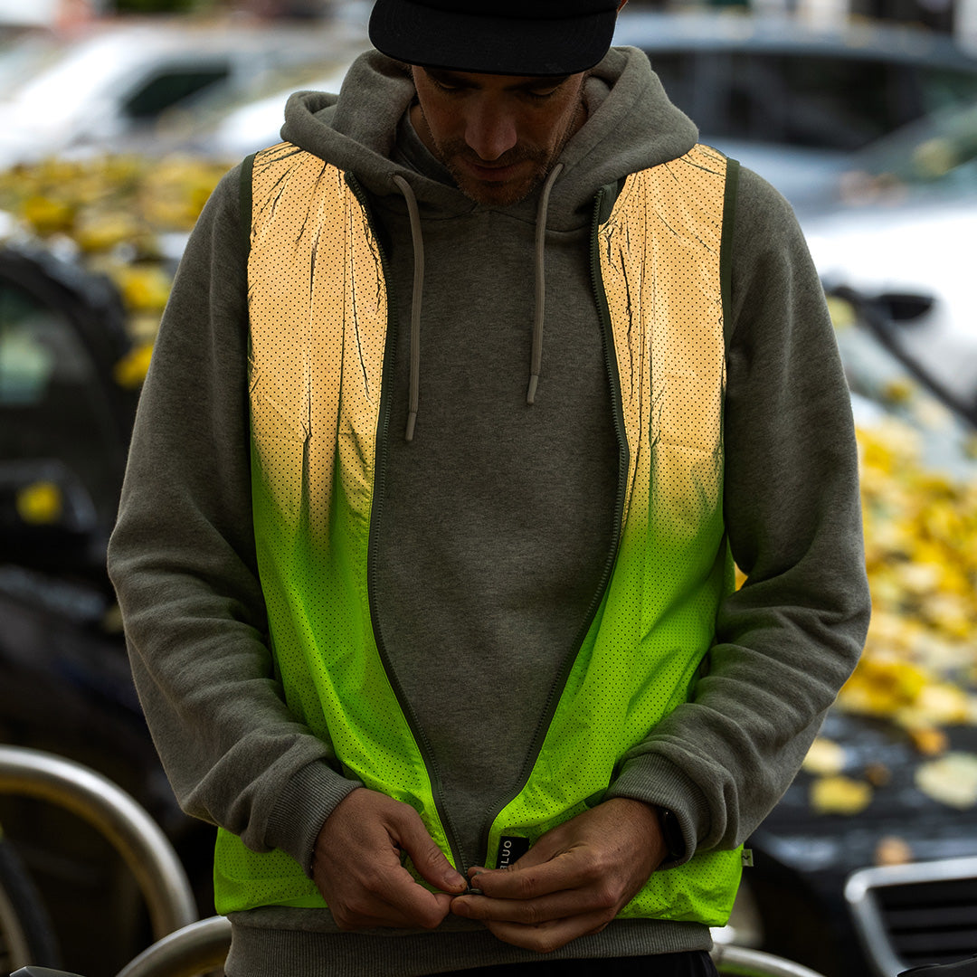 Man wearing green reflective vest in city with autumn leaves