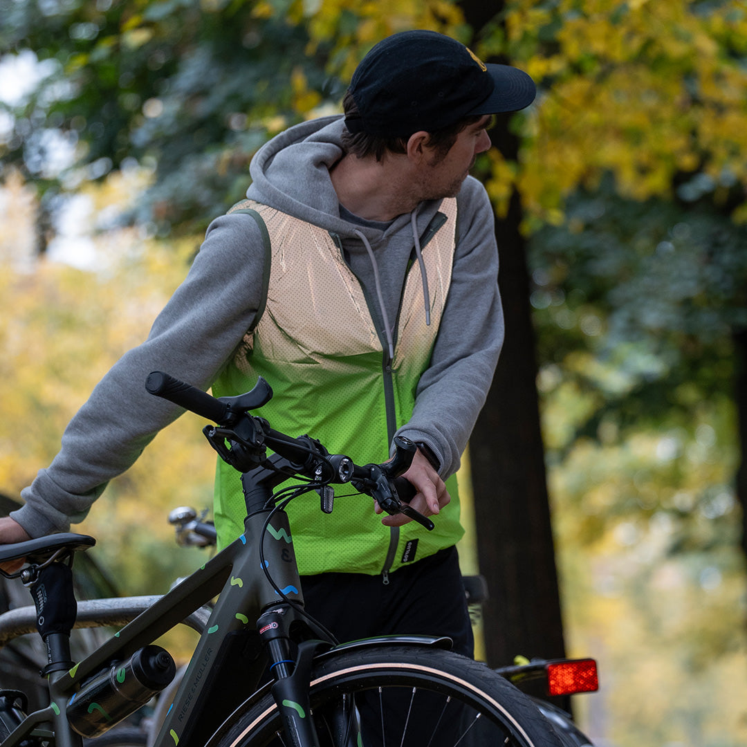 Man parking his bicycle and wearing a reflective vest with trees in background