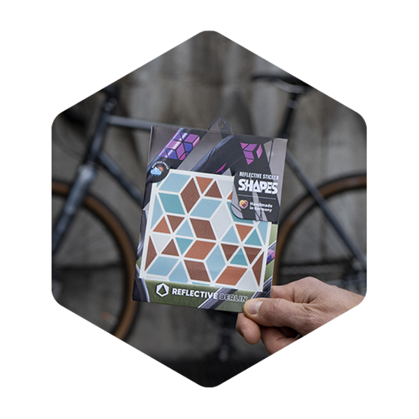 Eine Hand hält ein Sticker Produkt in der Hand. Im Hintergrund sieht man unscharf ein Fahrrad