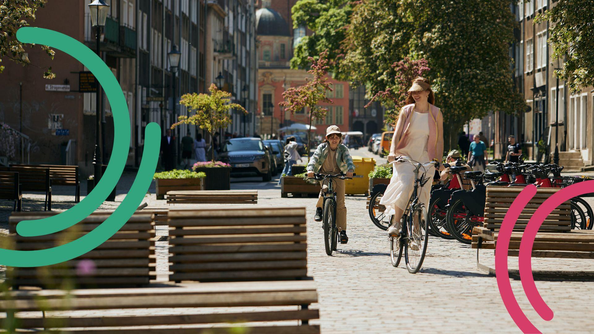 Frau und Kind mit Fahrrad radeln bei Sonnenschein über einen städtischen Platz