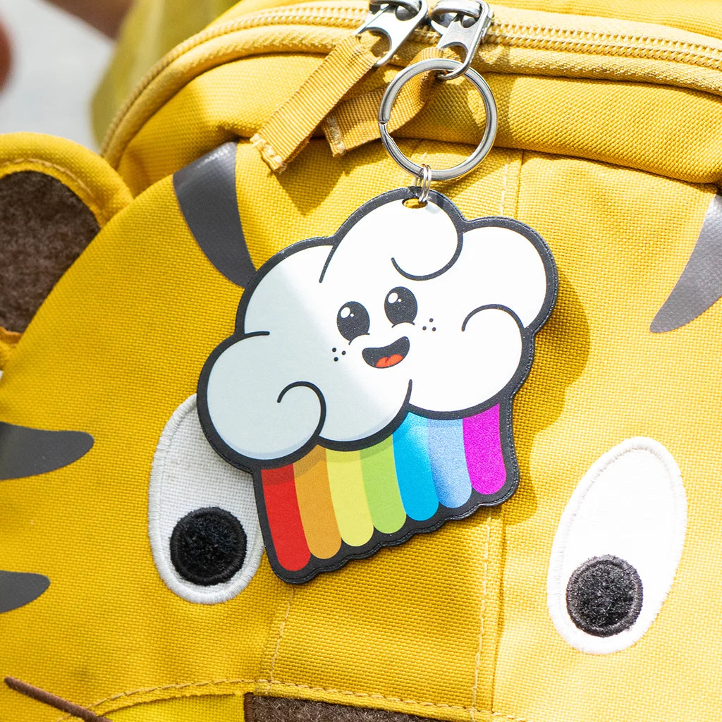 Reflektierender Anhänger ‚Reflective Hangers‘ in der Variante ‚Wolker’ - eine Wolke mit Regenbogen und einem lächelnden Gesicht. Der stark reflektierende Anhänger hängt an einem gelben Rucksack von REFLECTIVE Berlin.