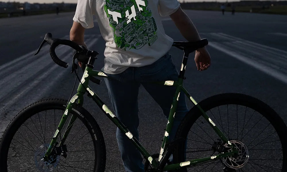 Reflektierende Aufkleber Tempelhofer Feld Themenwelt von REFLECTIVE Berlin auf einem grünen Gravelbike in der Gesamtansicht mit sichtbarer Reflexion und passendem T-Shirt aus der Kollektion auf dem Tempelhofer Feld.
