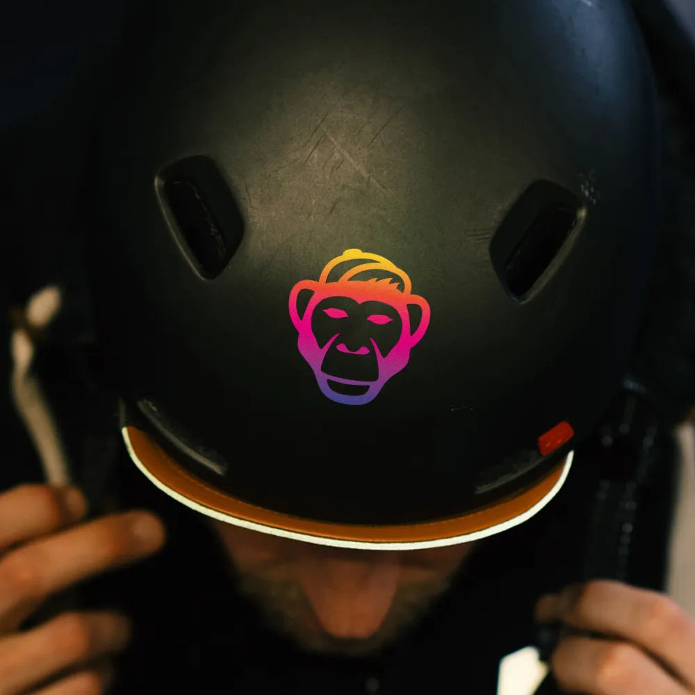 Reflektierender Aufkleber „Affe“ in Farbvariante „Regenbogen“ auf der Vorderseite von einem schwarzem Fahrradhelm von REFLECTIVE Berlin.