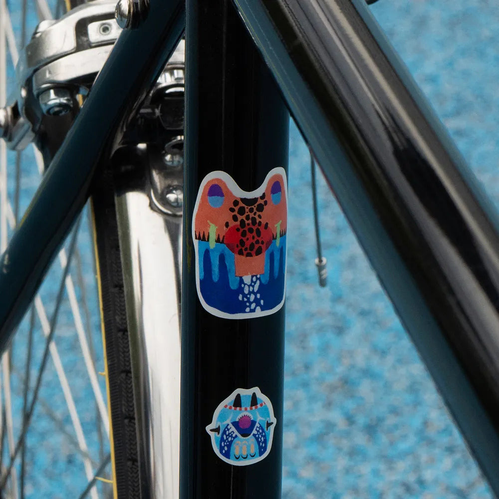Reflektierende Aufkleber Künstleredition „Kurihara“ auf schwarzem Fahrradrahmen. Zwei Aufkleber im Detail mit japanischen Masken. von REFLECTIVE Berlin