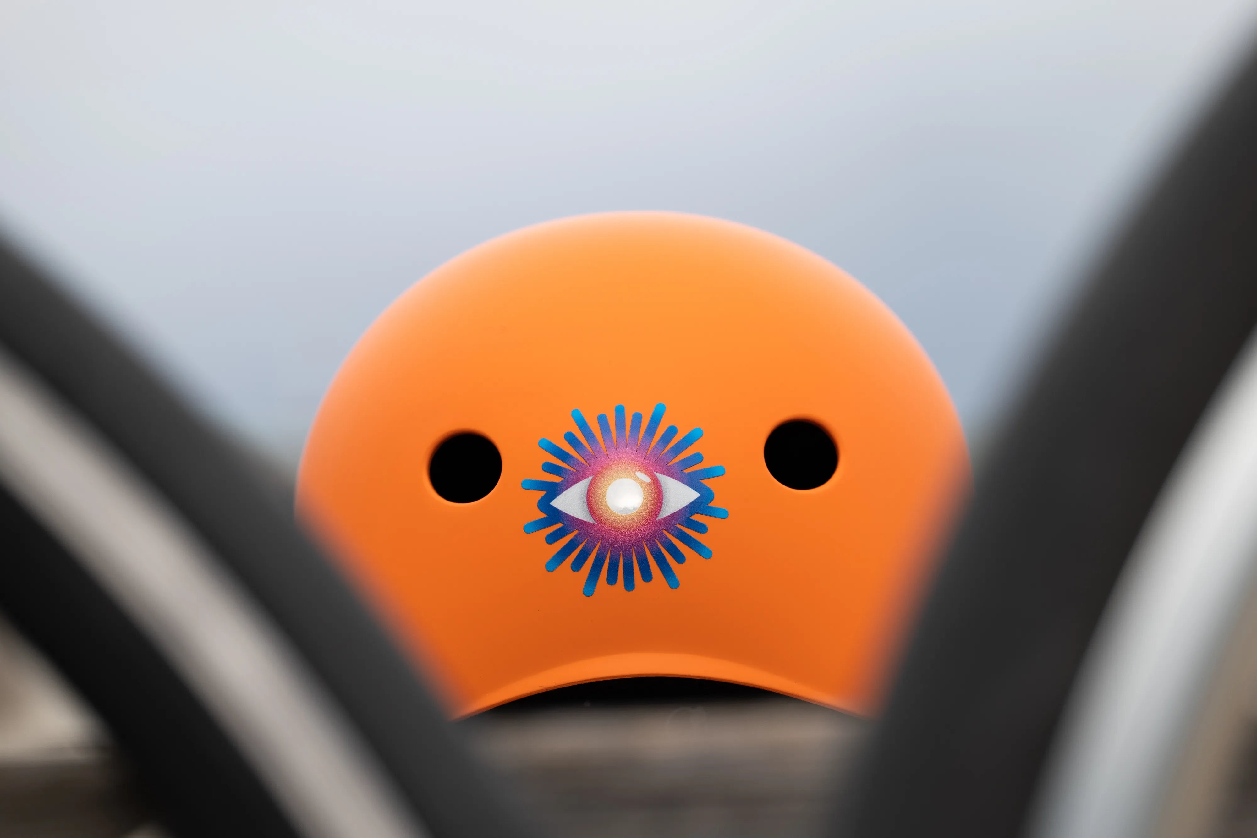 Reflektierender Aufkleber „Auge“ in Farbvariante „Regenbogen“ auf orangem Fahrradhelm Rückansicht. Von REFLECTIVE Berlin.