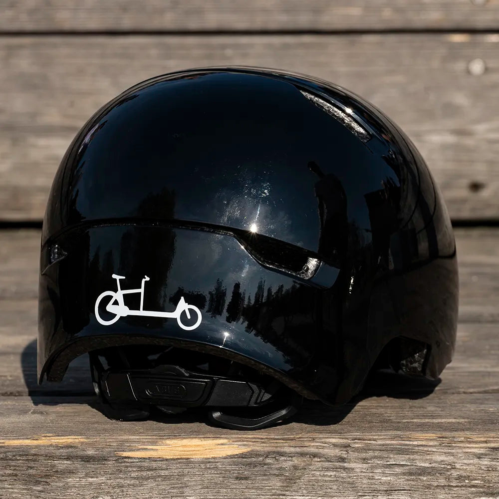 Reflektierender Aufkleber „Cargo“ in Farbvariante „weiß“ auf schwarzem Fahrradhelm vor unscharfem Hintergrund von REFLECTIVE Berlin.