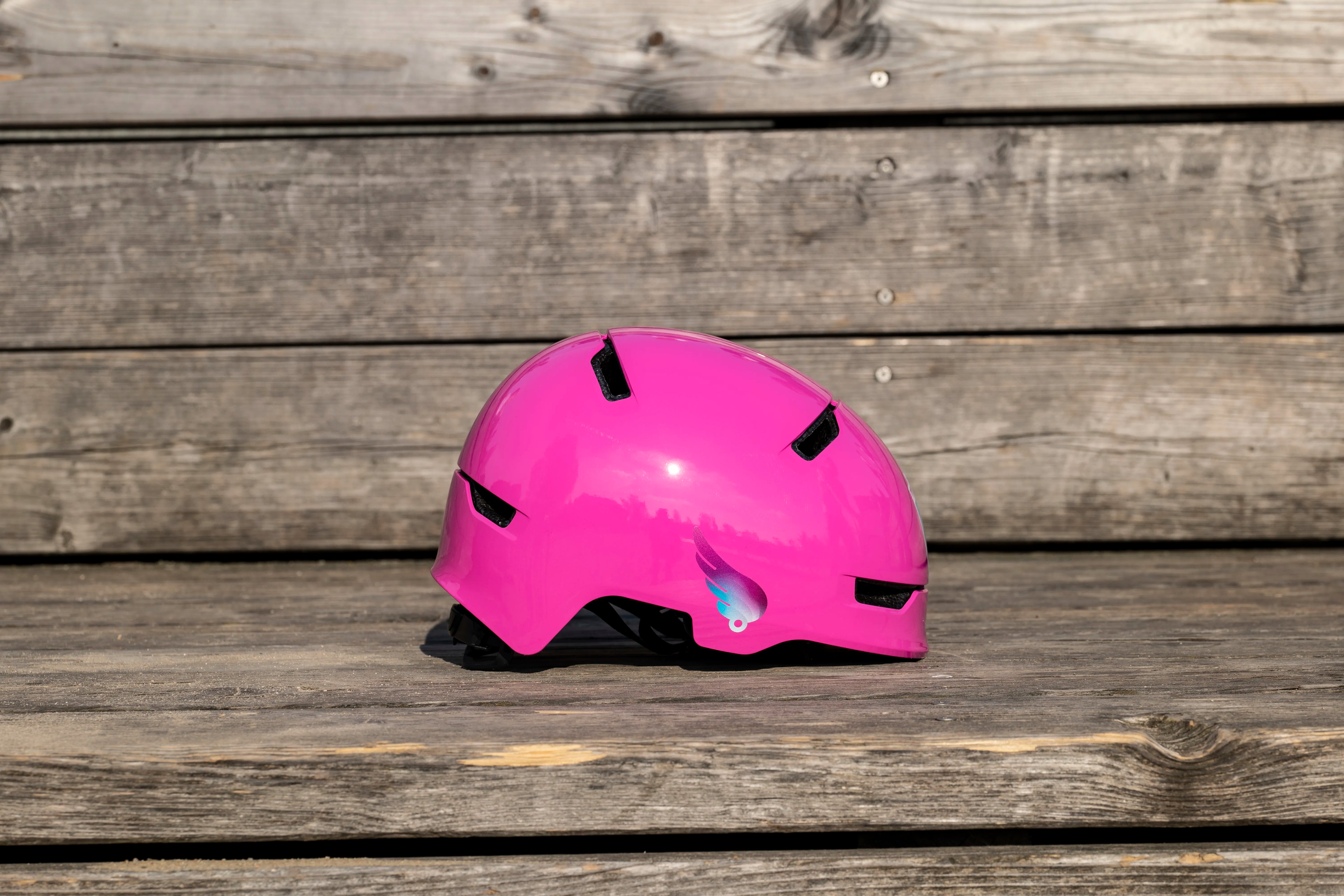 Reflektierender Aufkleber „Flügel“ in Farbvariante „Lila“ auf pinkem Fahrradhelm vor Holzhintergrund von REFLECTIVE Berlin