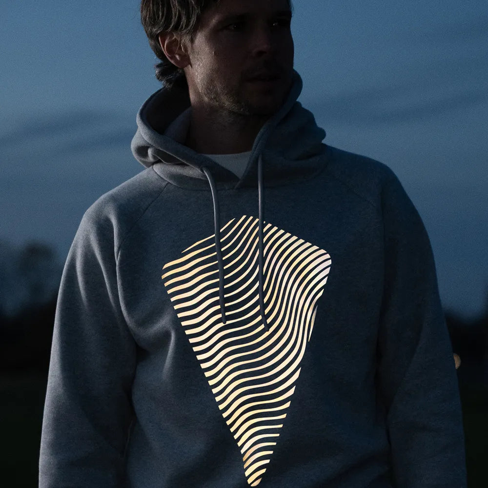 Person trägt den reflektierenden Hoodie Dune in Grau von REFLECTIVE Berlin bei Nacht mit sichtbarer Reflexion.