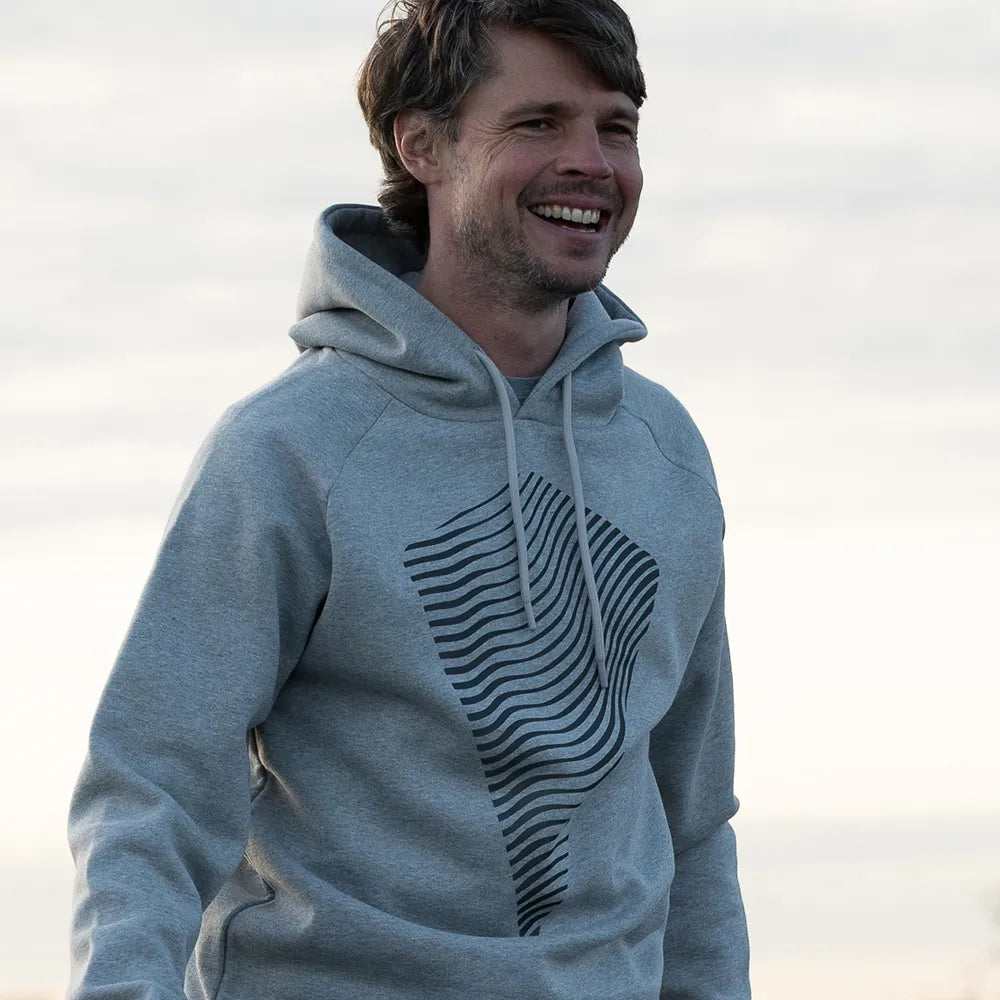 Lächelnde Person trägt den reflektierenden Hoodie Dune in Grau von REFLECTIVE Berlin auf dem Tempelhofer Feld bei Tageslicht.