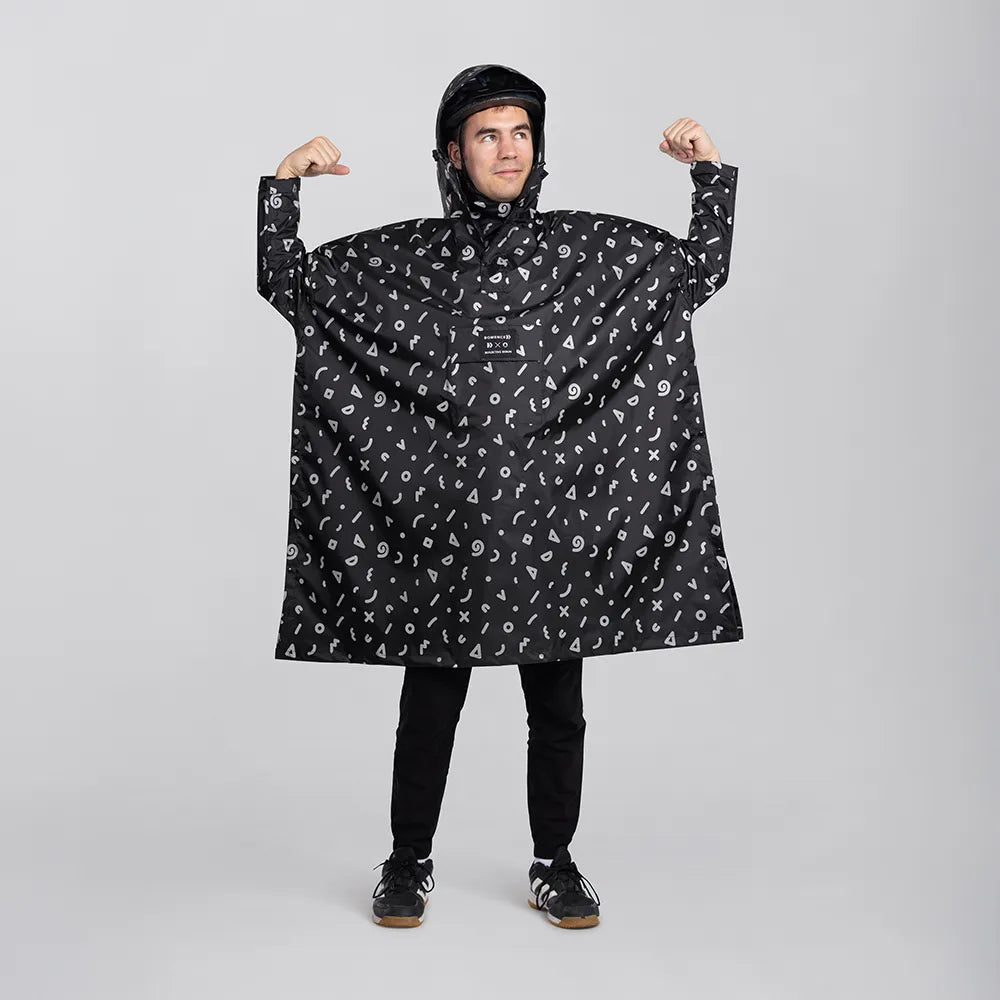 reflektierender Fahrrad Regenponcho in Farbvariante „Doodle“ getragen von einer Person, die frontal in die Kamera schaut und die Arme hebt, vor weißem Hintergrund. Kollaboration von Bomance und REFLECTIVE Berlin.