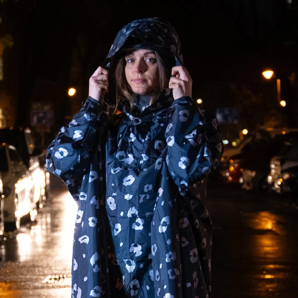 reflektierender Fahrrad Regenponcho in Farbvariante „Leo“, getragen von einer Person, die die Kapuze über den Kopf zieht. Das Bild wurde bei Dunkelheit mit Blitzlicht aufgenommen, um die Reflexion des Ponchos hervorzuheben. Kollaboration von Bomance und REFLECTIVE Berlin.