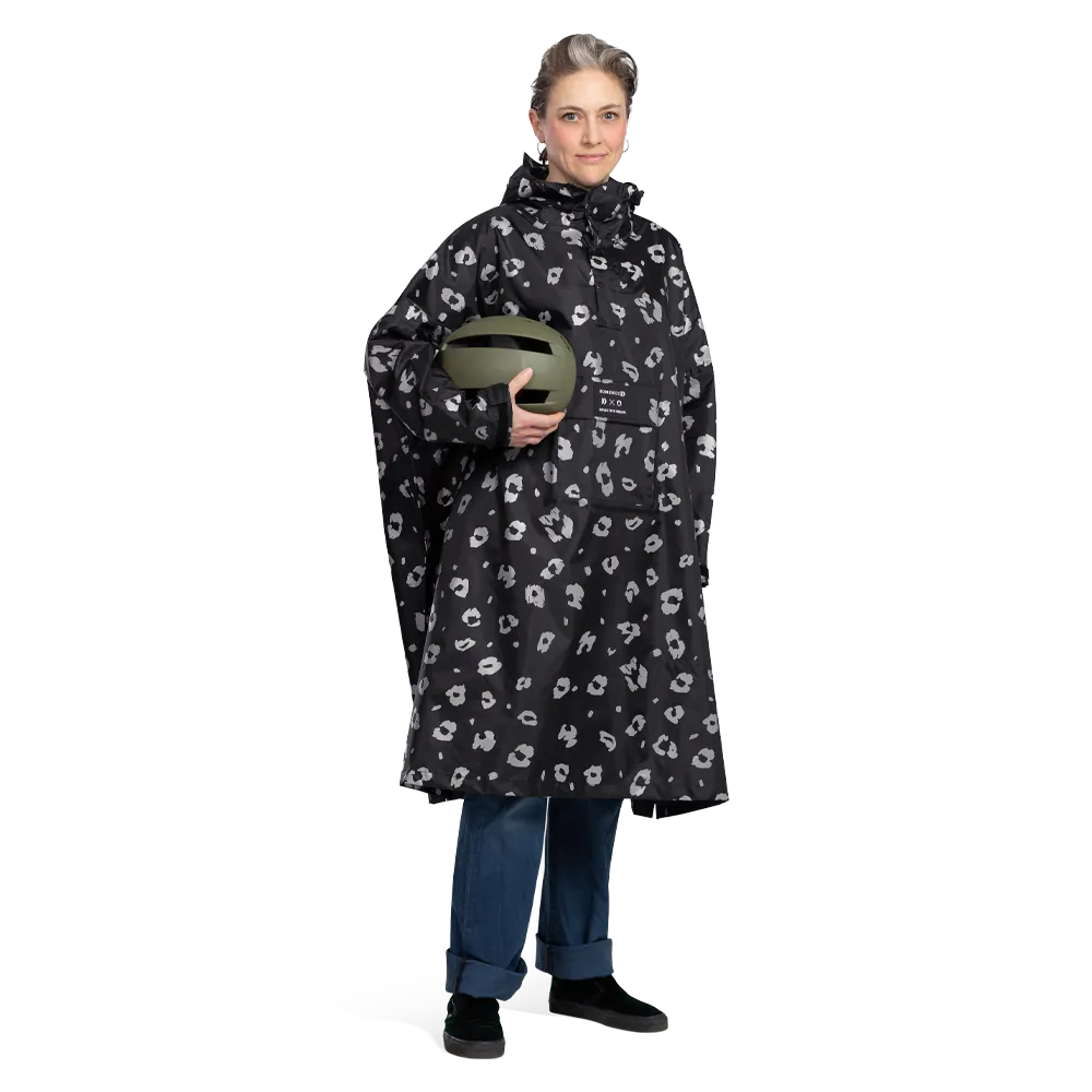 reflektierender Fahrrad Regenponcho in Farbvariante „Leo“ getragen von einer Person, die einen Helm in Oliv Farbe hält. Kollaboration von Bomance und REFLECTIVE Berlin.