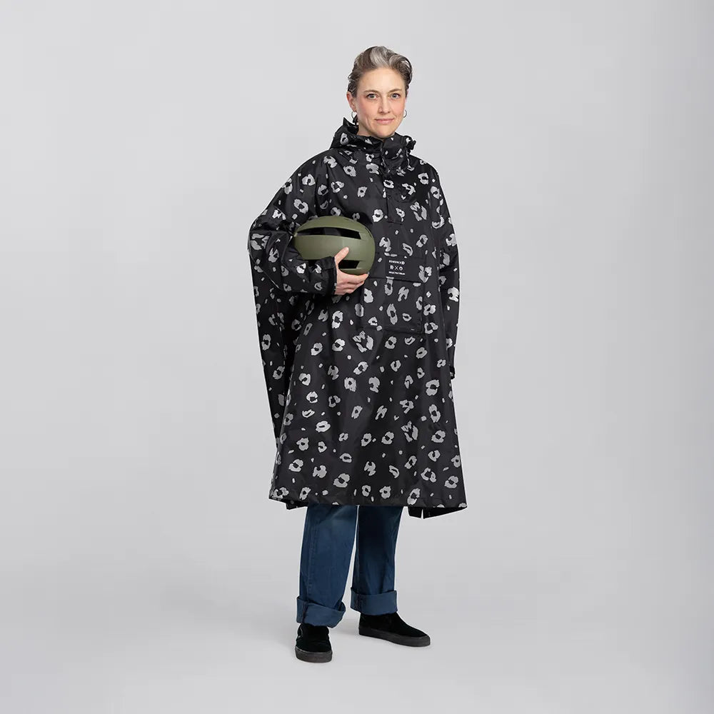 reflektierender Fahrrad Regenponcho in Farbvariante „Leo“, getragen von einer Person, einen grünen Fahrradhelm in der Hand hält. Kollaboration von Bomance und REFLECTIVE Berlin.