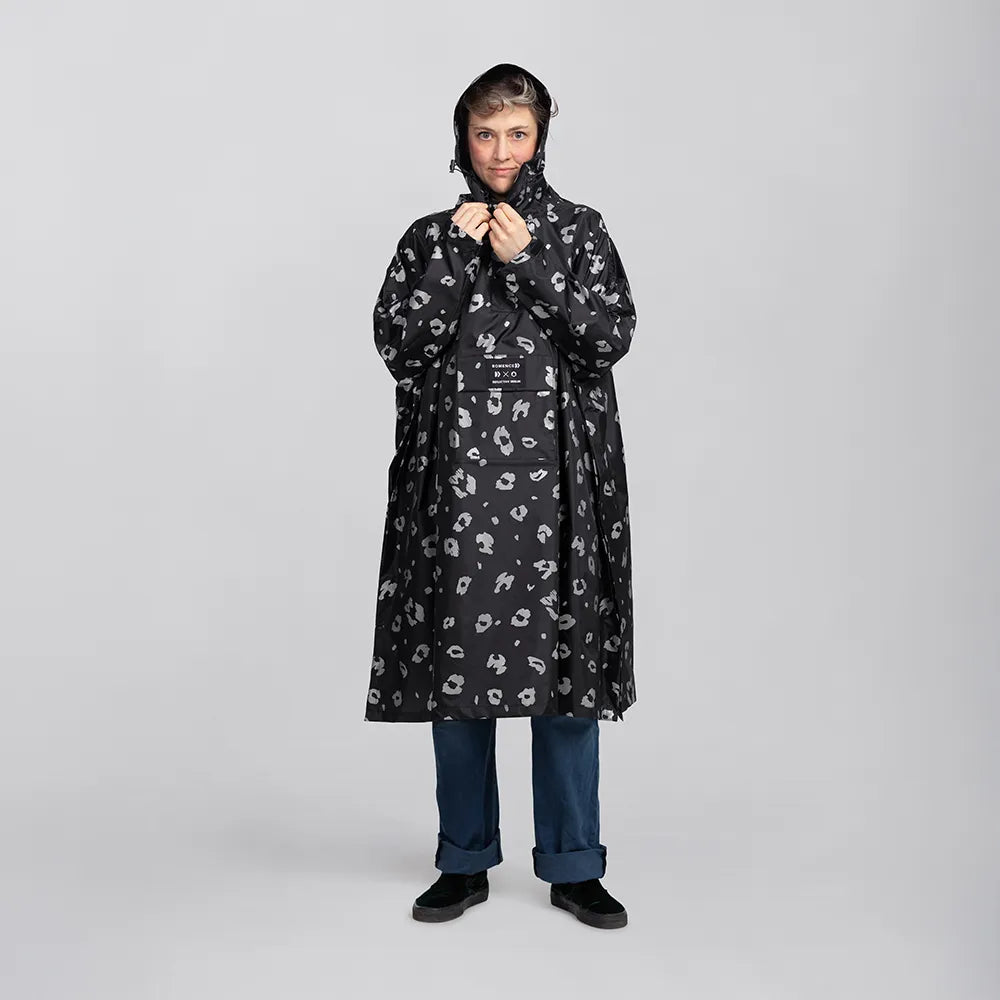 reflektierender Fahrrad Regenponcho in Farbvariante „Leo“, getragen von einer Person, die frontal in die Kamera schaut und Druckknöpfe des Ponchos zuknöpft. Kollaboration von Bomance und REFLECTIVE Berlin.