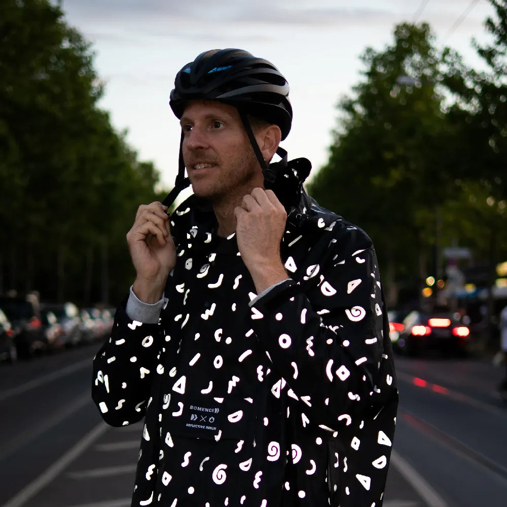 Detailaufnahme von stark reflektierenden Fahrrad Regenponcho in Farbvariante „Doodle“ getragen von einer Person, die einen Fahrradhelm trägt. Kollaboration von Bomance und REFLECTIVE Berlin.