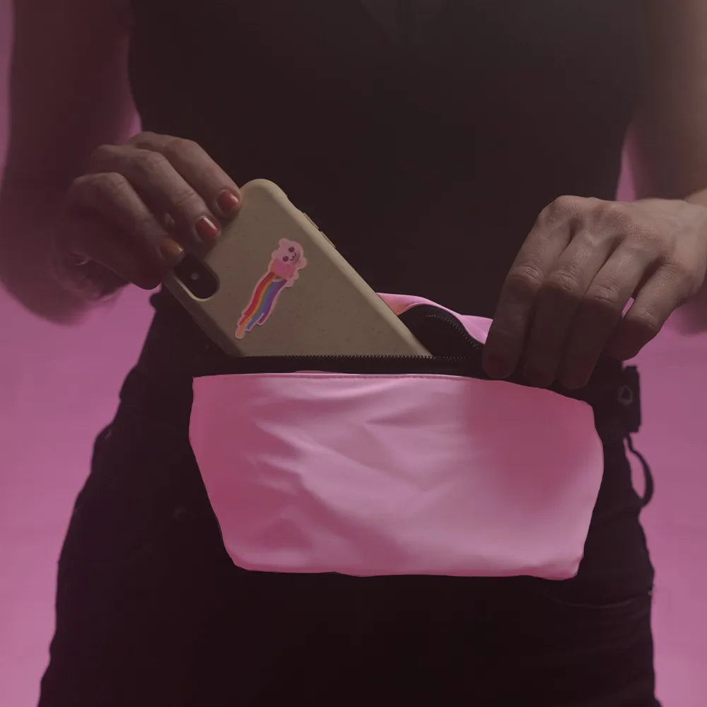 reflektierende Gürteltasche/Fanny pack/Pouch in Farbvariante „soft rosa“ die von einer Person um die Hüfte getragen wird. Die Person steckt ein Smartphone mit einem Nyan Cat Aufkleber in die reflektierende Gürteltasche. Arrangement mit hervorgehobener Reflexion von REFLECTIVE Berlin.