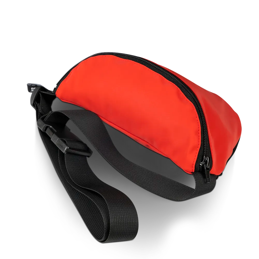 reflektierende Gürteltasche/fanny pack/Pouch in Farbvariante „Tomato red“ in Seitenansicht, die Trägerriemen und Klipp-Verschluss der Tasche zeigt. Arrangement von REFLECTIVE Berlin.