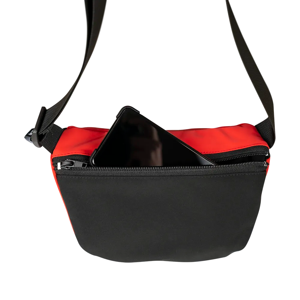 reflektierende Gürteltasche/fanny pack/Pouch in Farbvariante „Tomato red“ in Rückansicht. Ein Smartphone schaut teilweise aus der Rücktasche mit Reißverschluss heraus. Arrangement von REFLECTIVE Berlin.