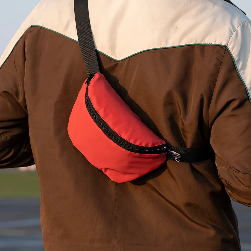 reflektierende Gürteltasche/fanny pack/Pouch in Farbvariante „Tomato red“ wird von einer Person auf dem Rücken getragen. Arrangement bei Tageslicht von REFLECTIVE Berlin.