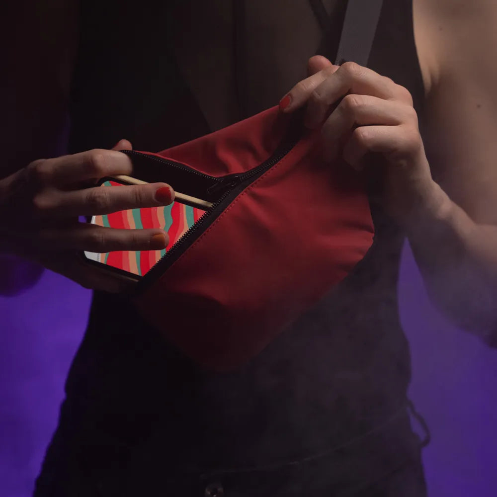 reflektierende Gürteltasche/fanny pack/Pouch in Farbvariante „Tomato red“ wird von einer Person am Oberkörper getragen. Ein Smartphone wird in die Fronttasche gesteckt. Arrangement von REFLECTIVE Berlin.