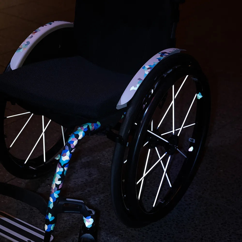 Reflektierender Speichen Aufkleber „Spokes“ in Farbvariante „weiß“ auf den Speichen von einem Rollstuhl. Auf dem Rahmen sind reflektierende Aufkleber „DIY“ in Farbvariante „vitrail“ verklebt. Von REFLECTIVE Berlin.