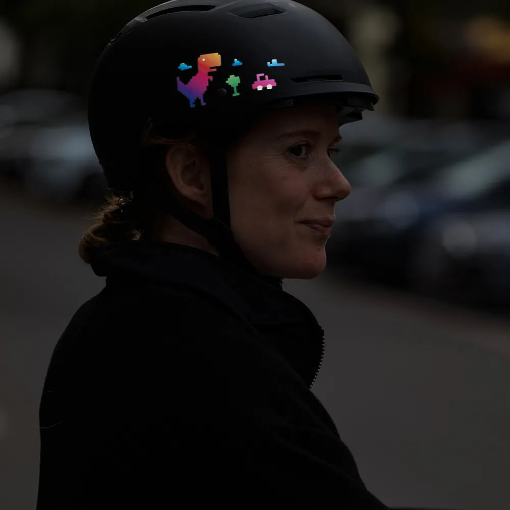 Reflektierender Aufkleber „T-Rex“ in Farbvariante „Regenbogen“ auf schwarzem Fahrradhelm der von einer Person getragen wird. Von REFLECTIVE Berlin.