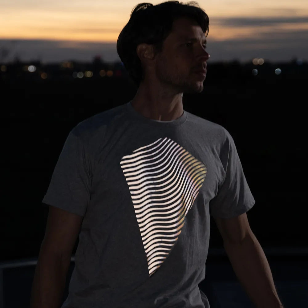 Person schaut nach rechts, trägt das reflektierende T-Shirt Dune in Grau von REFLECTIVE Berlin bei Sonnenuntergang.