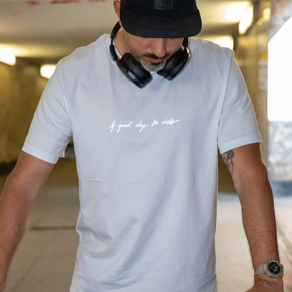 Person mit schwarzer Cap trägt das T-Shirt Streetlife in Weiß von REFLECTIVE Berlin in einer U-Bahn Unterführung bei Tageslicht. Der Slogan „A good day to ride“ reflektiert stark.