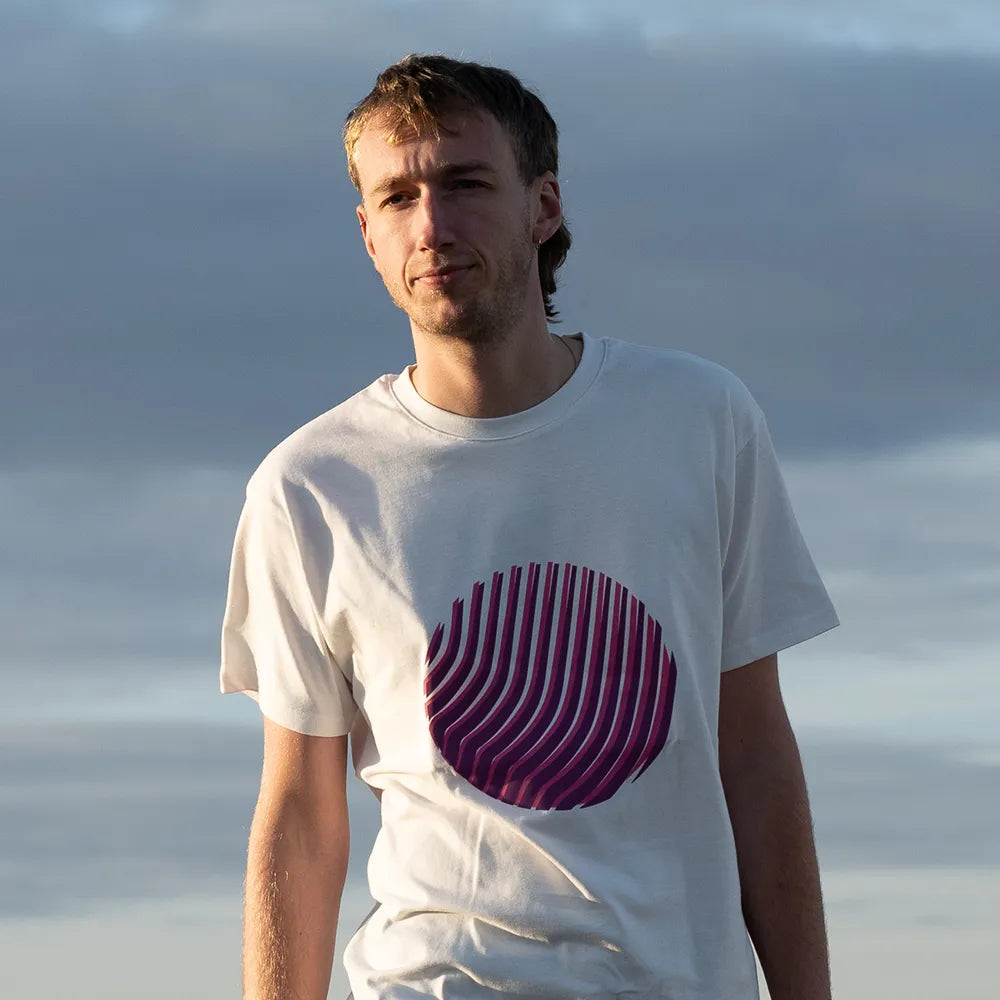 Person trägt das reflektierende T-Shirt Sunset in Off-white mit pinkem Print von REFLECTIVE Berlin im Freien bei Tageslicht.