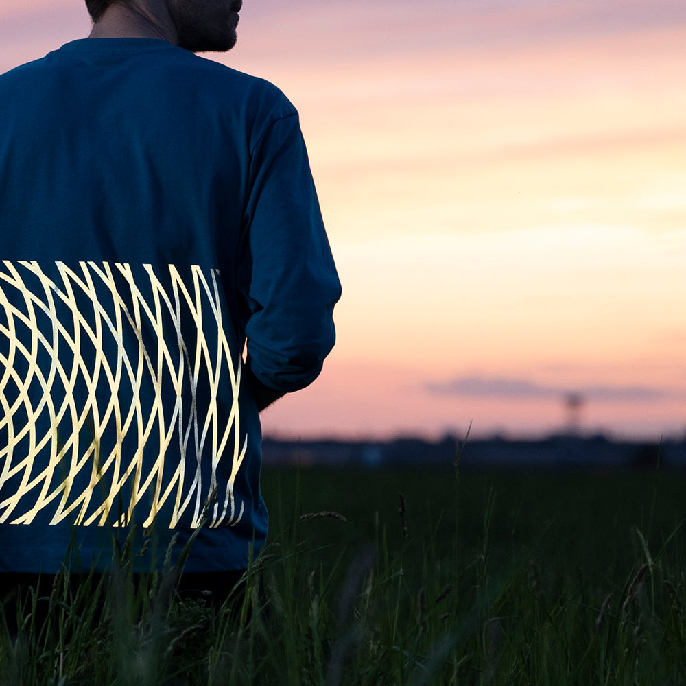 linke Hälfte Rückseite von Typ mit leuchtendem Aufdruck auf Rücken von Pulli, rechts Sonnenuntergang und Weite