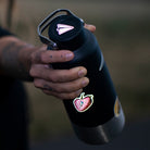hand holding a metal water bottle with a reflective paperplane design