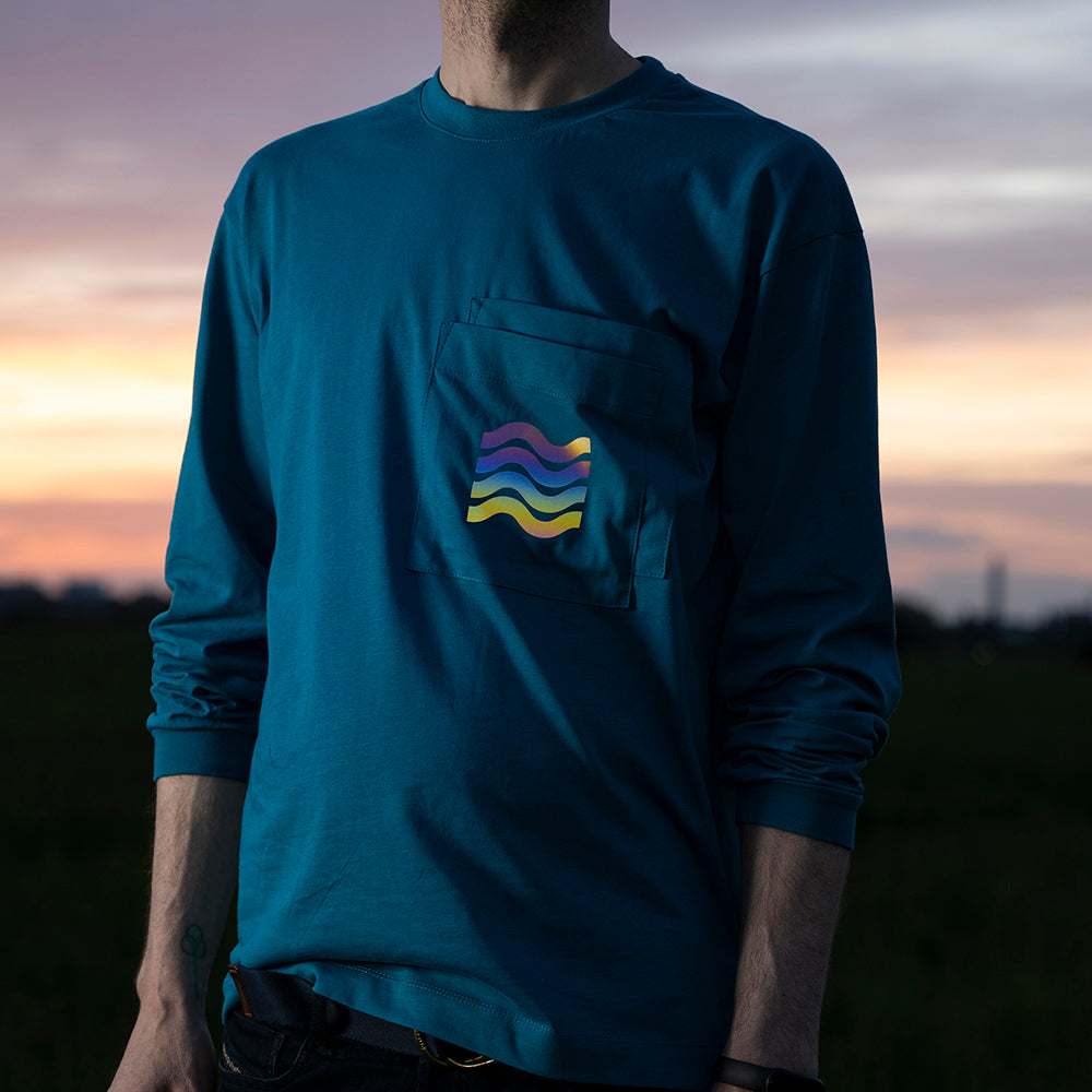 Mann trägt Longsleeve mit hochgekrempelten Ärmeln, auf den Brusttaschen sind bunt reflektierende Wellen aufgedruckt