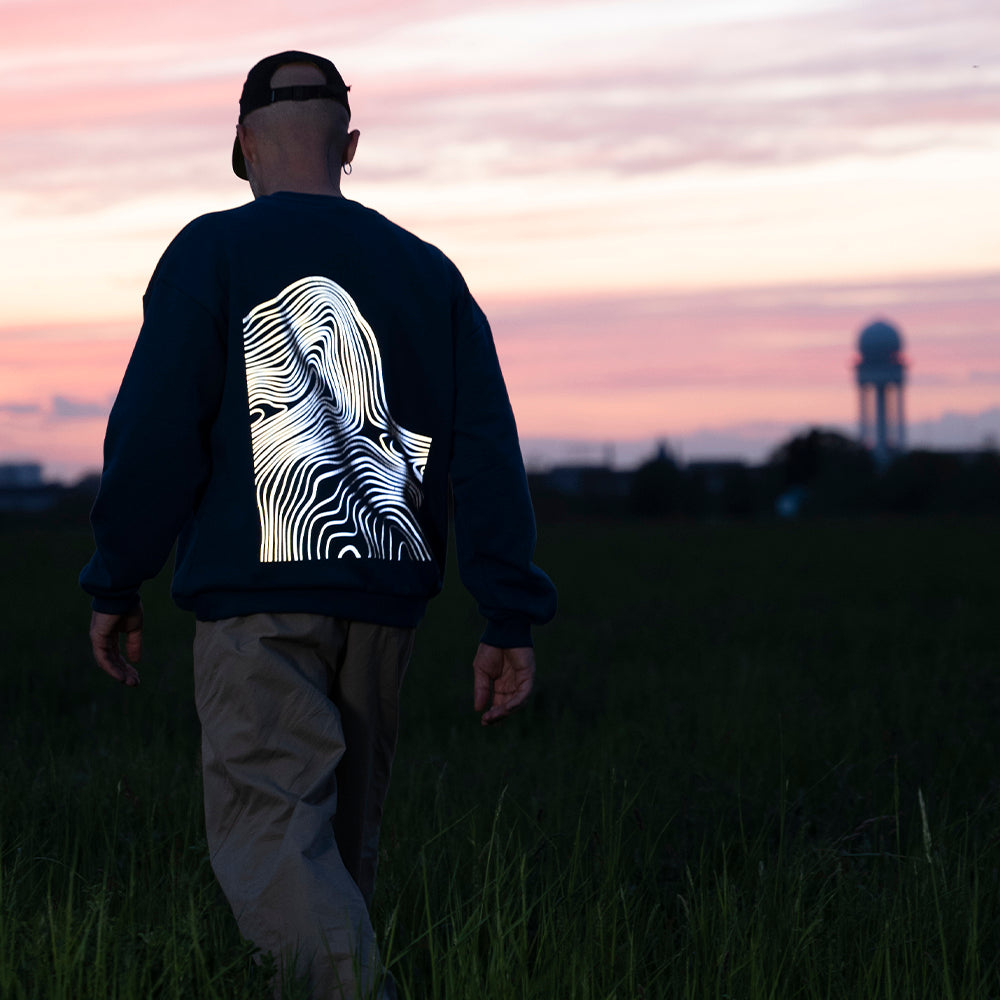 Typ geht über Wiese, Pullover reflektiert am Rücken stark