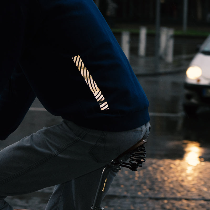 Fahrradfahrer auf Sattel sitzend, linke Ansicht, Auto mit Scheinwerfern im HintergrundReflective Hoodie, back print