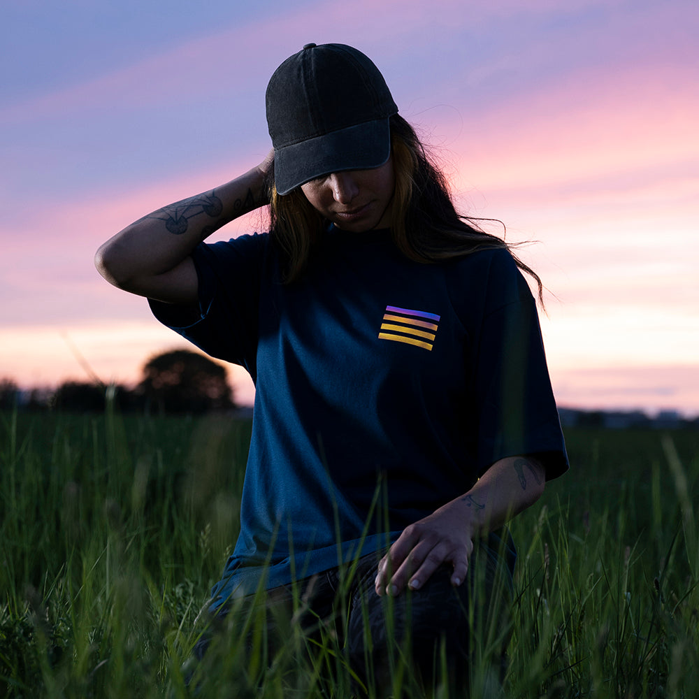 tättowiertes Mädchen mit Cap im Gras, schaut nach unten, rechter Arm hinterm Kopf