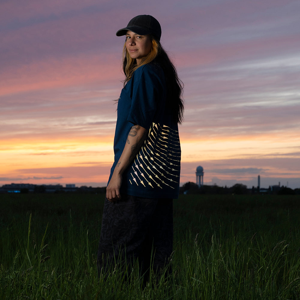 Frau vor Sonnenuntergang auf Wiese dreht sich seitlich zur Kamera, T-Shirt reflektiert stark