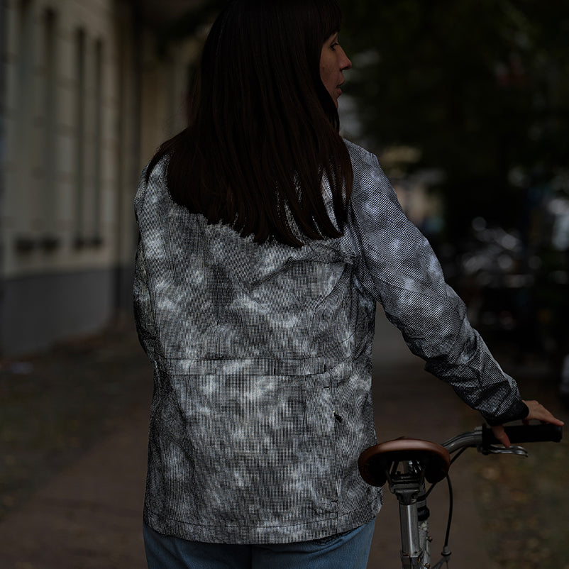 woman wearing reflective jacket, walking with bicycle