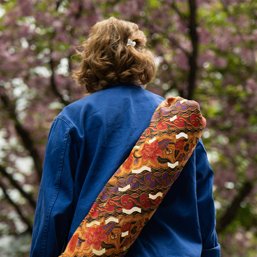 woman with yoga matt bag on her shoulder and tree in background with blur