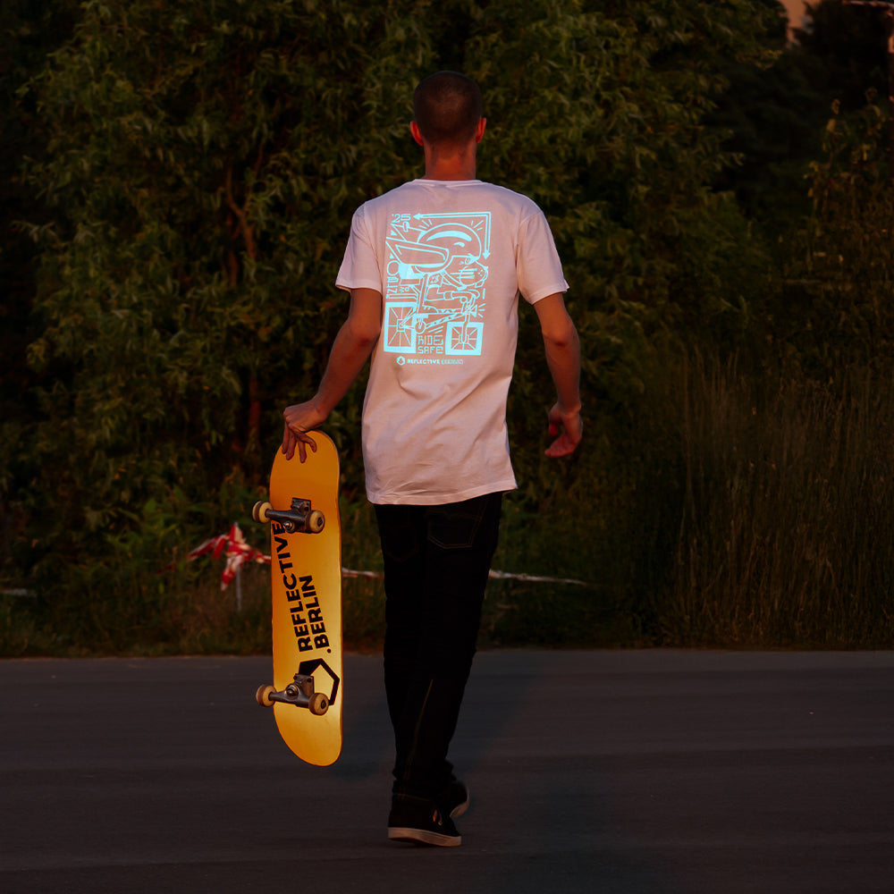 Man wearing reflective t-shirt and holding a skateboard on street.