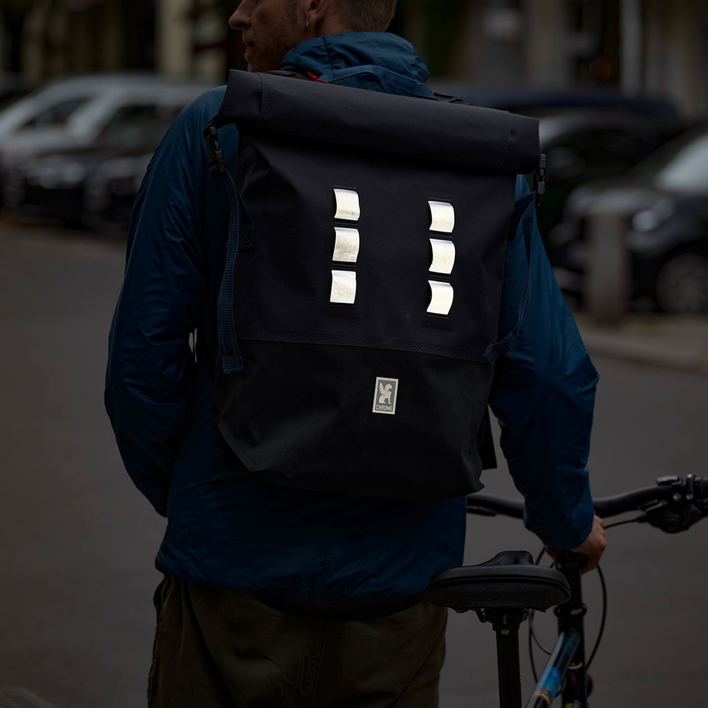 man pushing a bike and wearing chrome backpack with reflective lugs