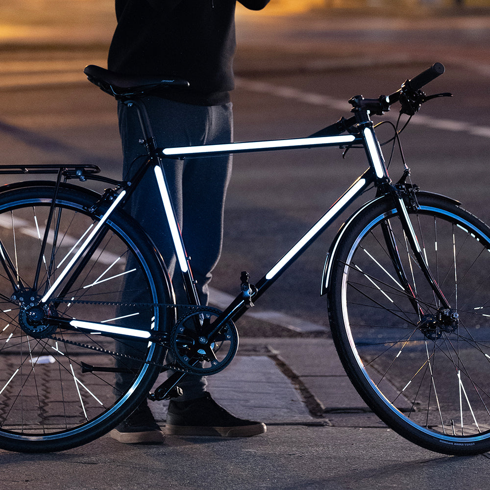 Schwarzes Fahrrad mit reflektierenden Streifen steht auf der Straße im Dunkeln, dahinter der Besitzer