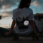 Woman sitting on skateboard with sky background and reflective smiley design on t-shirt
