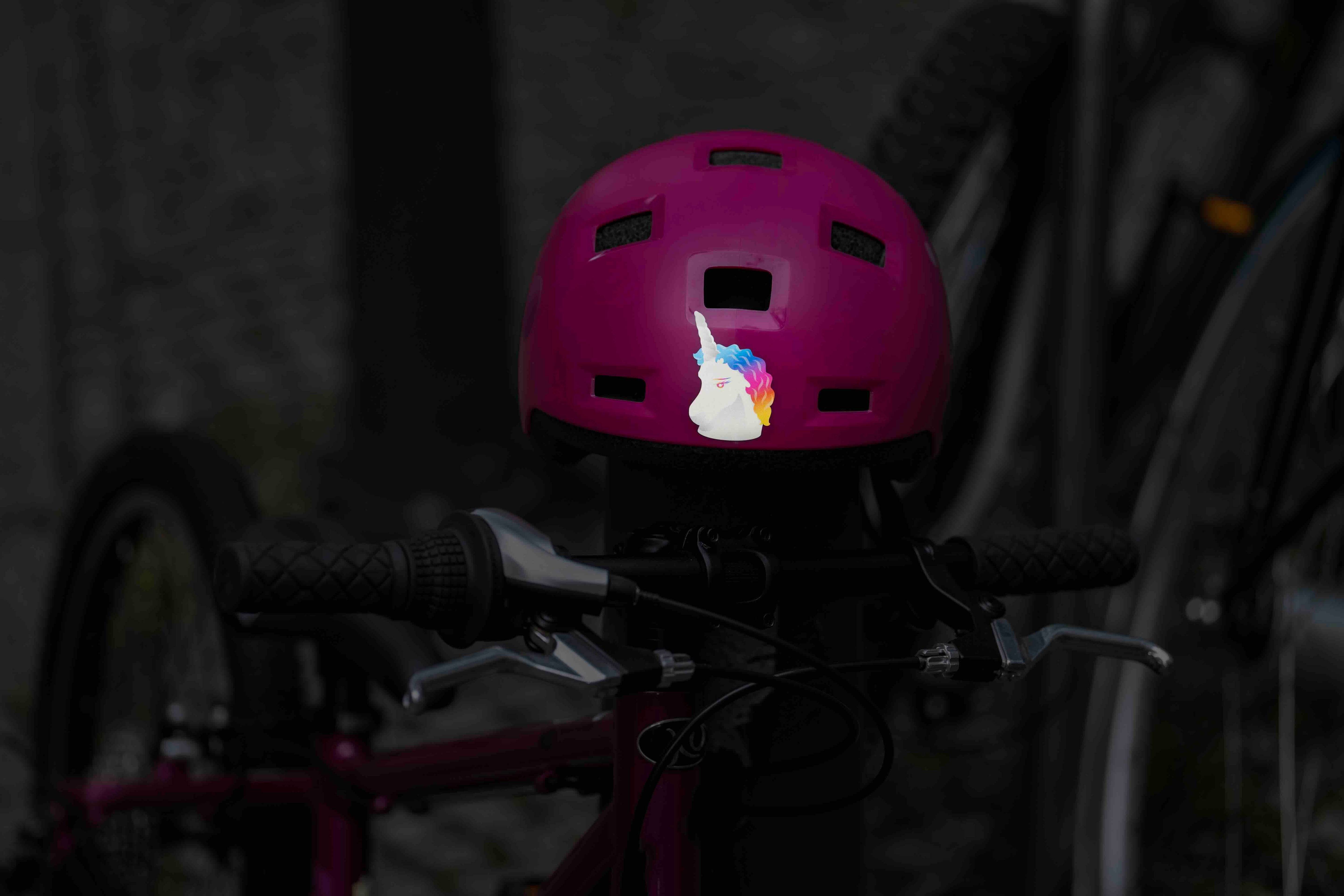 Einhorn Regenbogen von REFLECTIVE Berlin auf rosafarbenem Helm mit stark reflektierendem mehrfarbigem Einhornmotiv und rosa Fahrrad im Hintergrund.