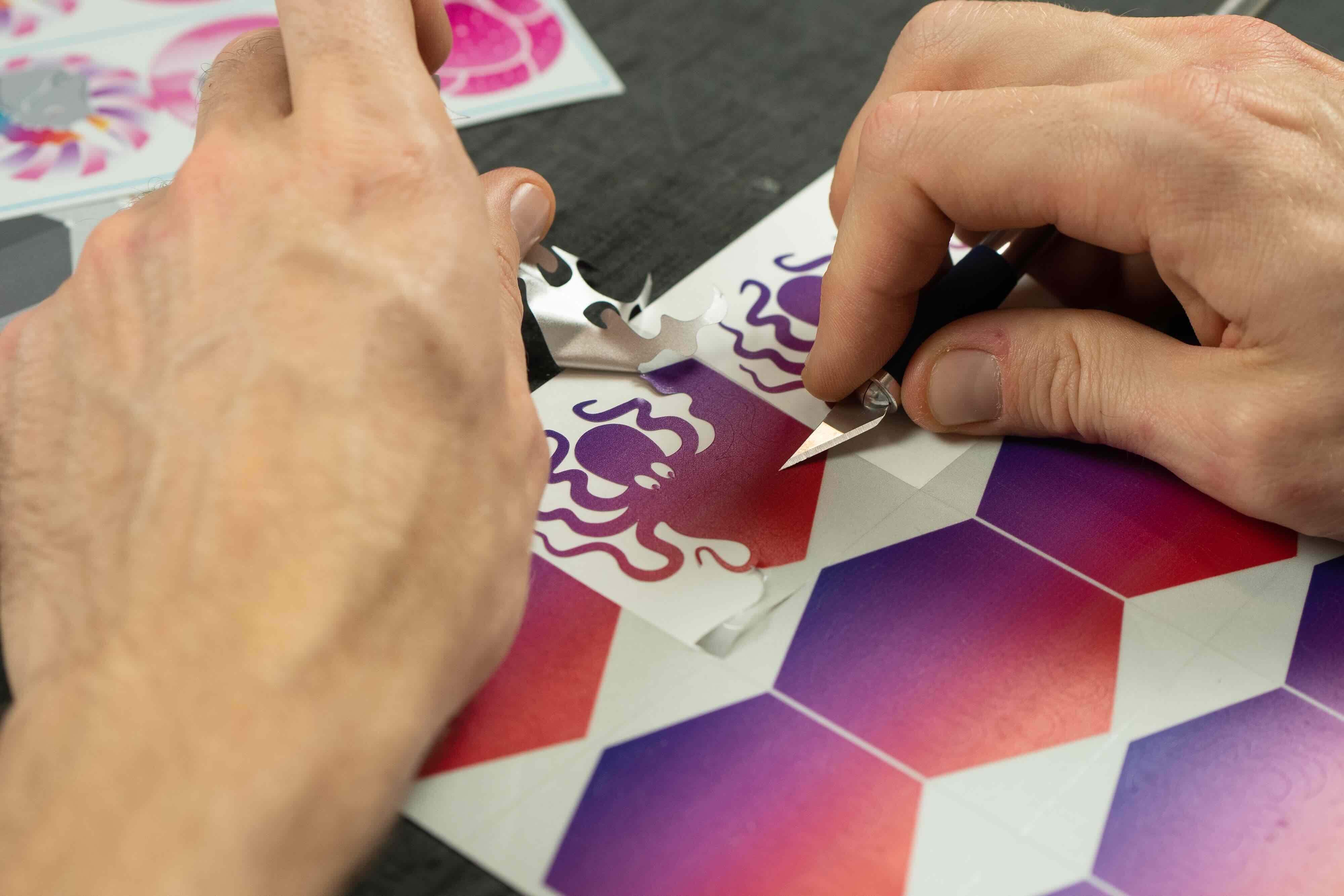 Einblick in die Produktion von REFLECTIVE Berlin, zwei Hände entgittern sorgfältig einen reflektierenden Oktopus-Decal auf Stickerbögen.