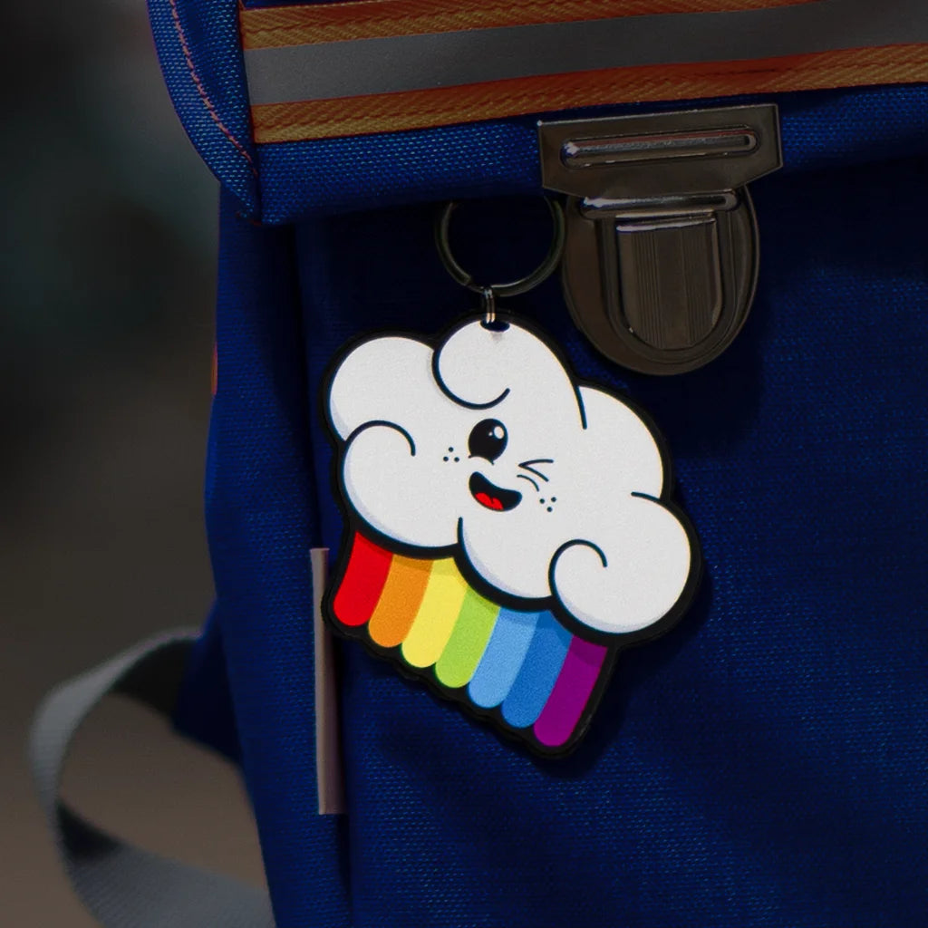 Reflektierende Anhänger ‚Reflective Hangers‘  in der Variante ‚Wolker’ - eine Woke mit Regenbogen und einem lächelnden Gesicht. Der stark reflektierende Anhänger hängt an einem blauen Rucksack von REFLECTIVE Berlin.