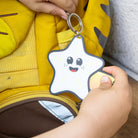 Reflektierender Anhänger ‚Reflective Hangers‘  in der Variante ‚Sterni’ - ein lächelnder Stern mit Sternschweif. Der stark reflektierende Anhänger wird von Kinderhänden an einem Rucksack befestigt. Produktbilder von REFLECTIVE Berlin.
