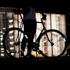 Reflektierender Felgen Aufkleber „Racer“ in Farbvariante „weiß“ in Größe 40mm auf schwarzem Fahrrad Felgen im Dunkeln mit verschwommenen Lichtern im Hintergrund. von REFLECTIVE Berlin. 