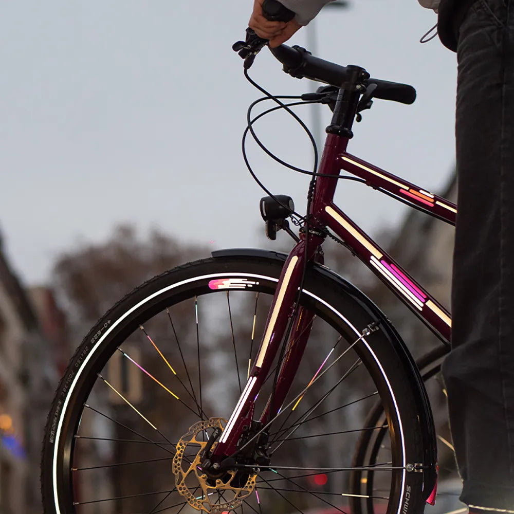 Reflektierender Aufkleber „Smudge“ in Farbvariante „pink“ auf Fahrradfelge. Reflektierender Aufkleber „Universal“ in Farbvarianten „weiß“ und „pink“ auf Fahrradrahmen. Speichen beklebt mit Aufkleber „Spokes“ in Farbvariante „Regenbogen" von REFLECTIVE Berlin.