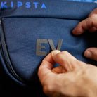 Reflektierende Aufkleber Textil Stoff „DIY“ in Farbvariante „Grau“ in Form geschnitten zu Buchstaben E und V, die von einer Hand auf einen KIPSTA Rucksack geklebt werden. Sticker von REFLECTIVE Berlin.